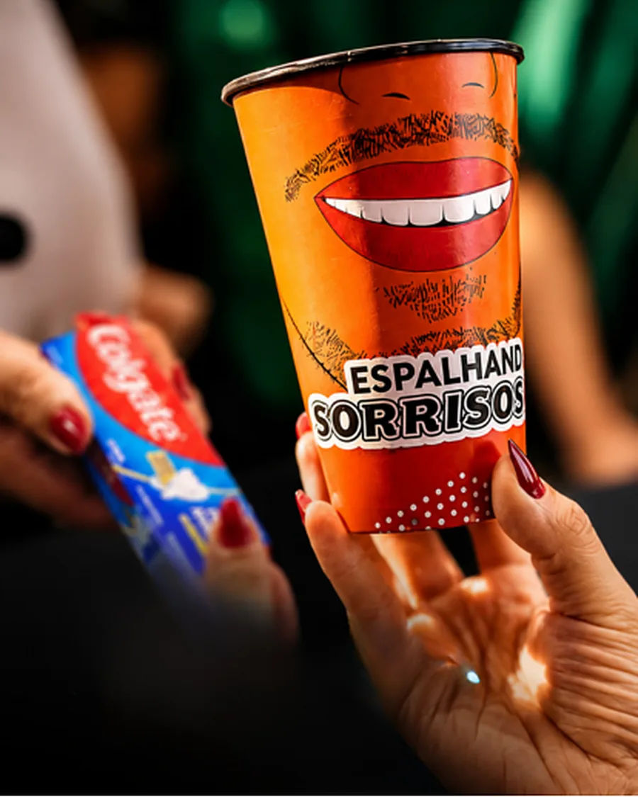 Mão segurando um copo laranja com a arte Espalhando Sorrisos em uma ativação de marca
